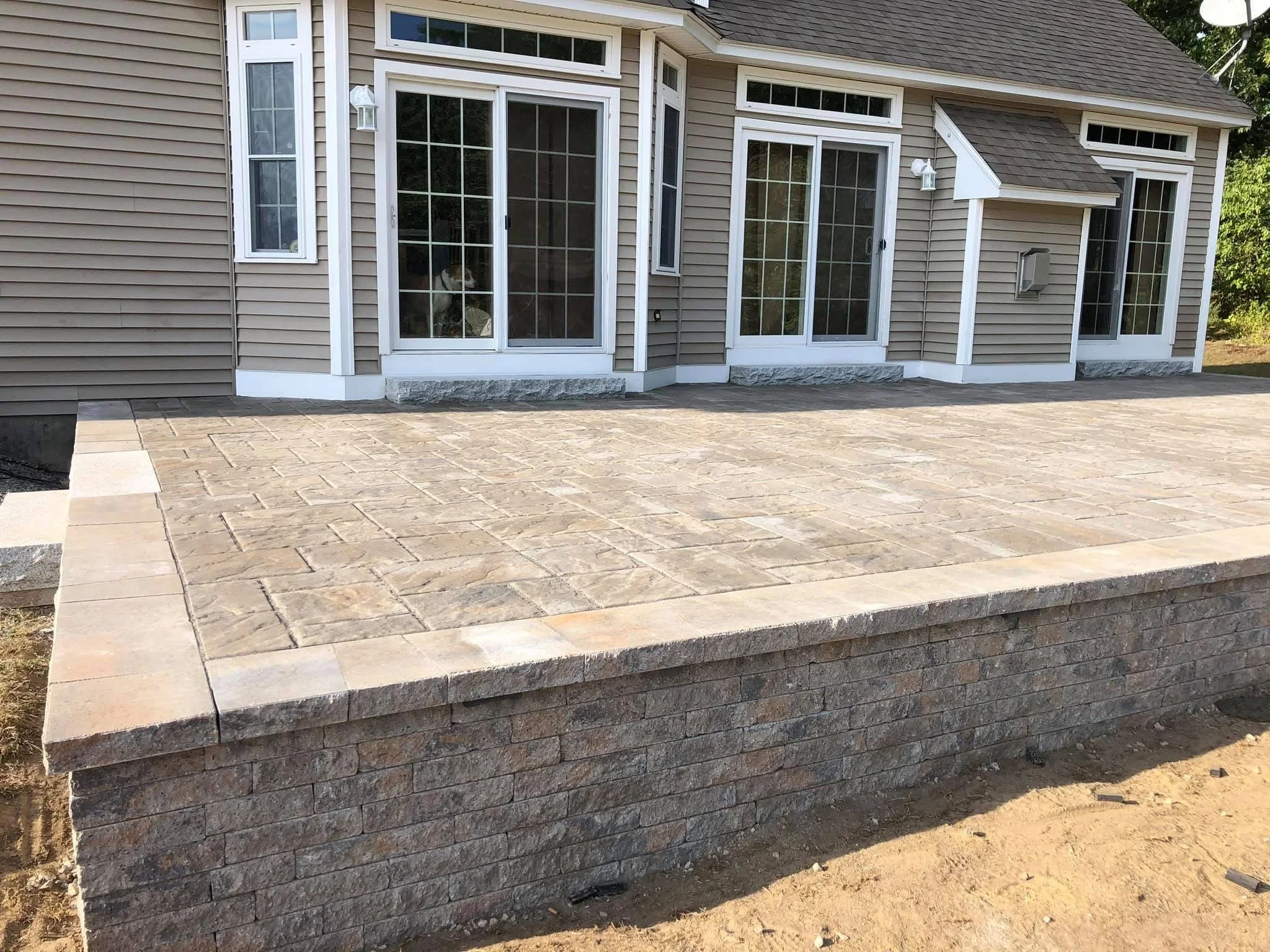 Raised stone retaining wall with herringbone paver patio overlooking residential home