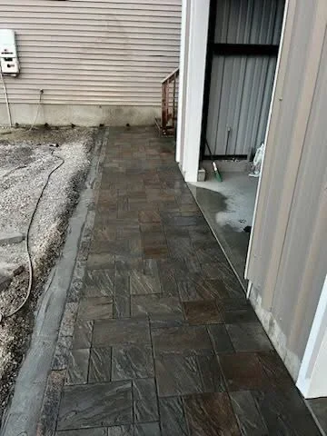 Charcoal paver walkway in herringbone pattern along residential building foundation