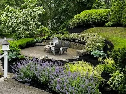 Stone patio with Adirondack chairs surrounded by lavender, boxwood hedges, and tiered plantings