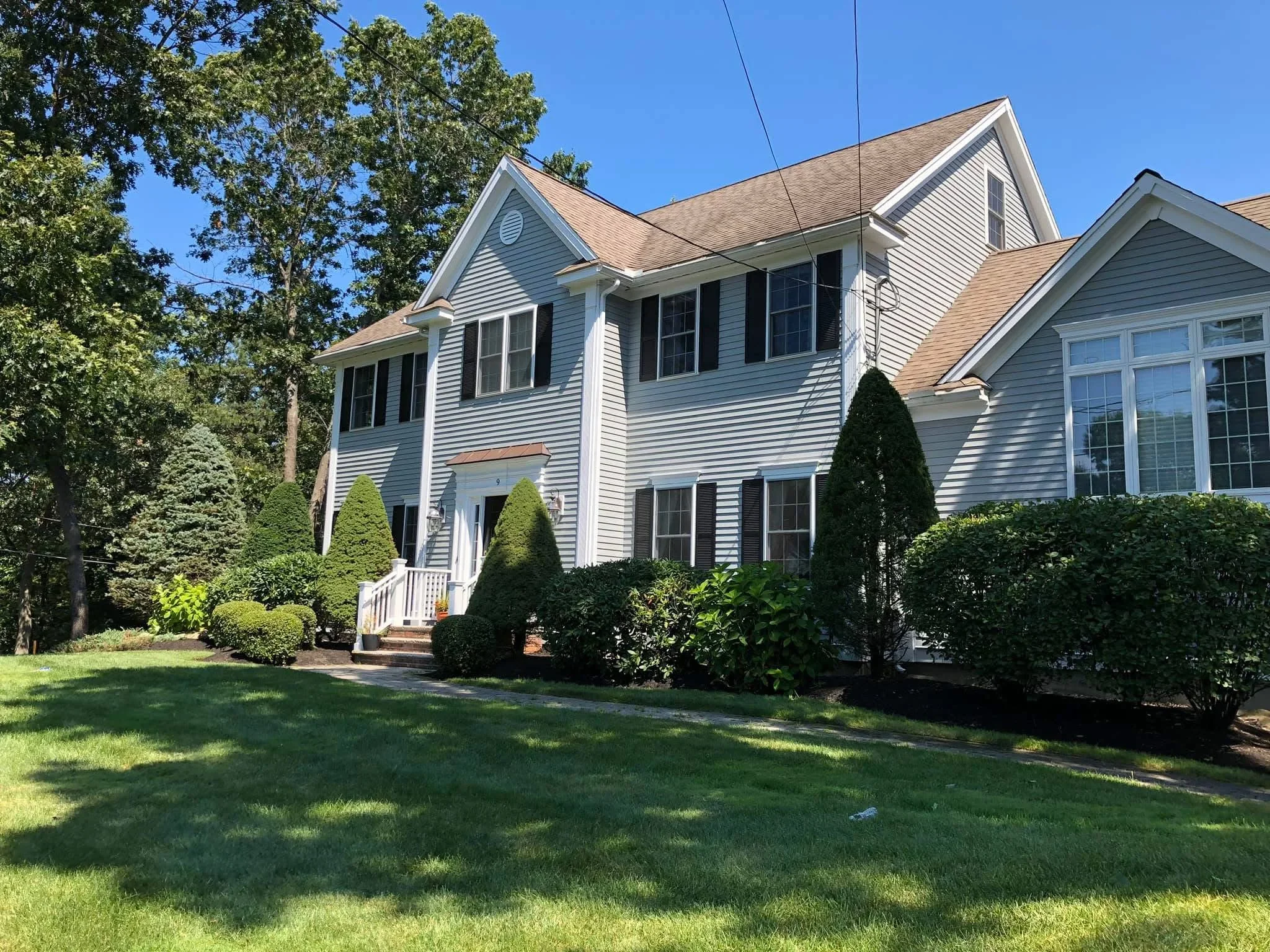 Manicured evergreen shrubs and hedging around colonial home with white siding