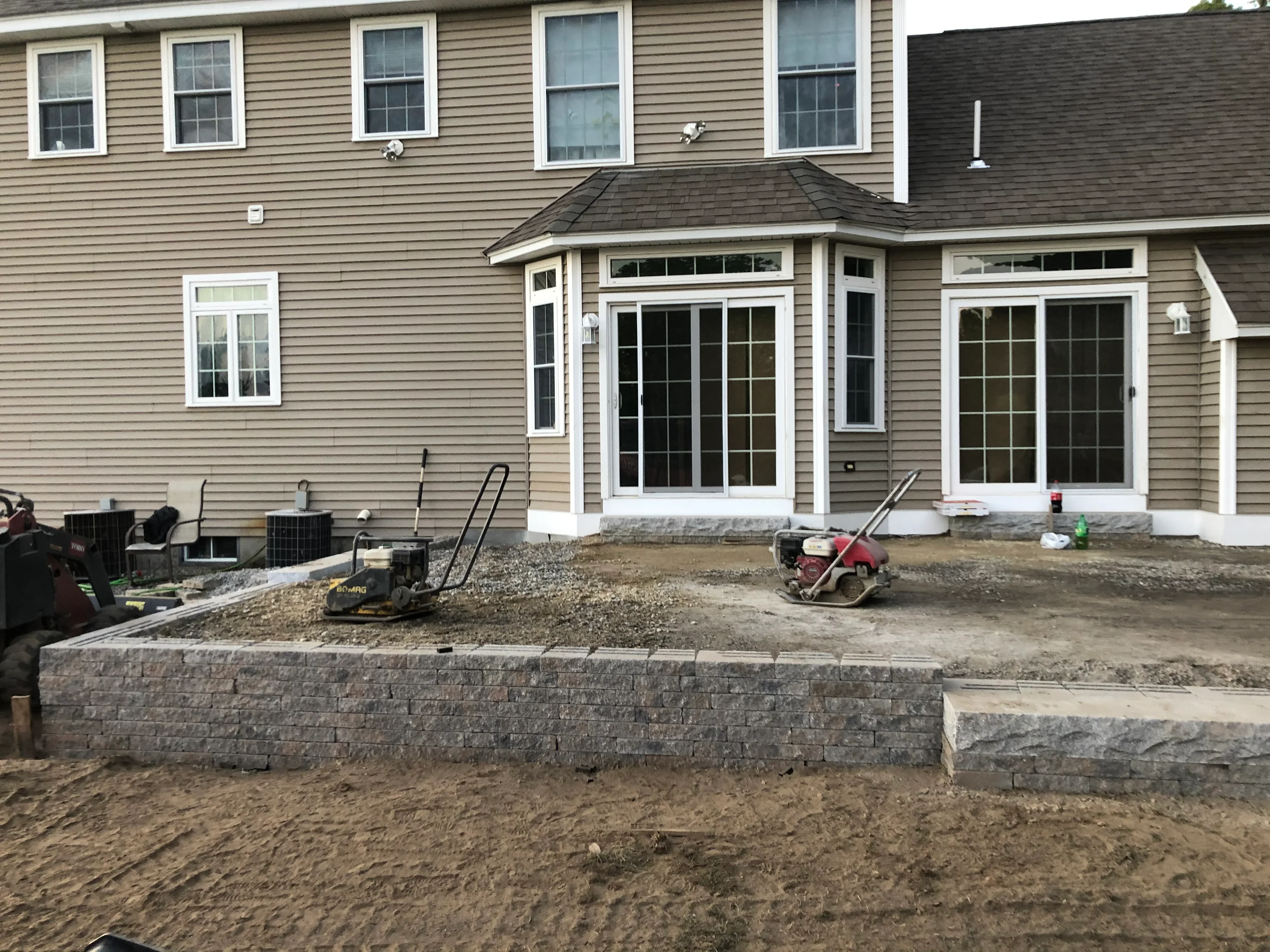 Gray segmental retaining wall and graded patio area under construction at residential home