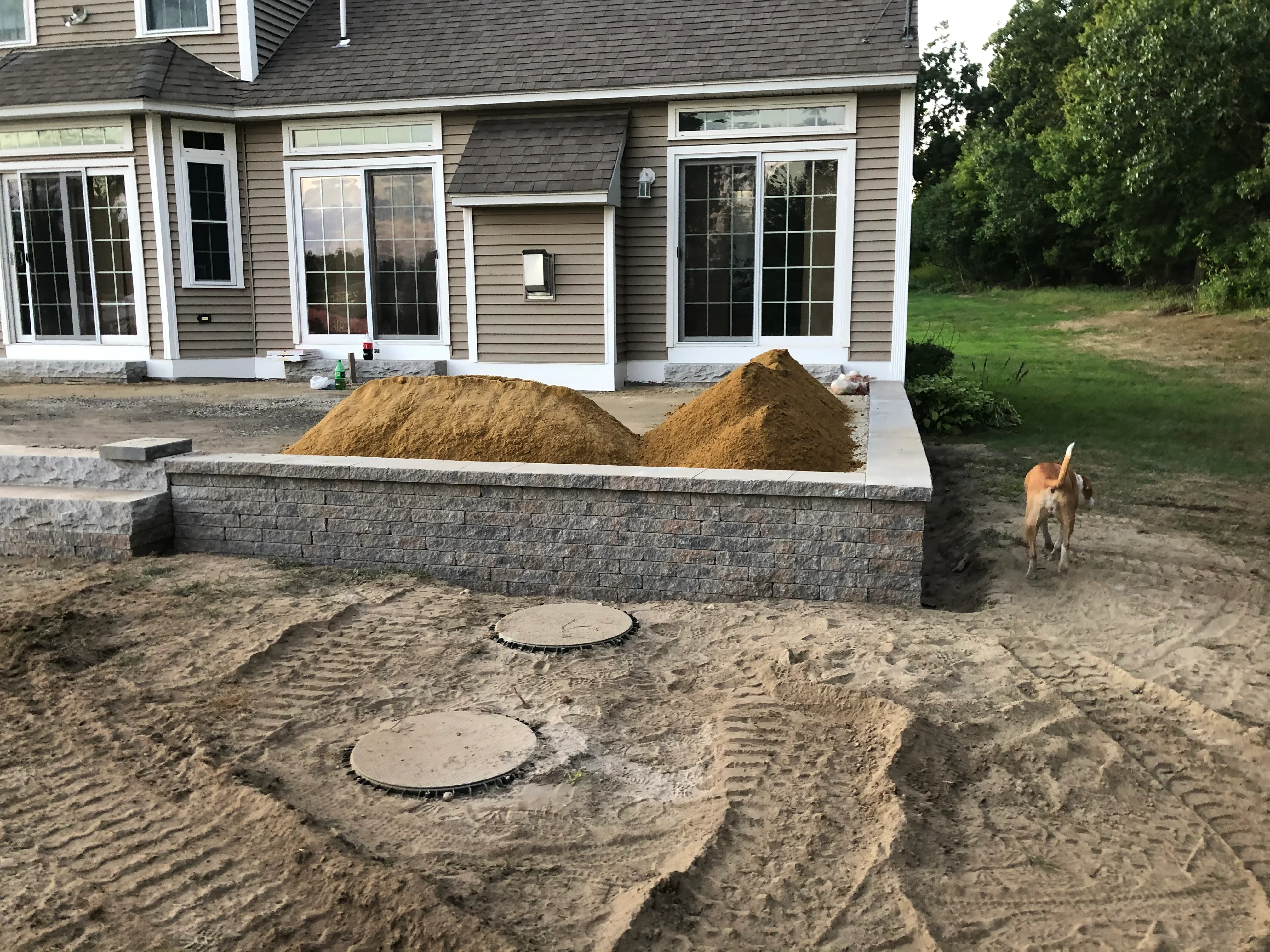 Segmental retaining wall with stone facing and graded soil preparation around residential foundation
