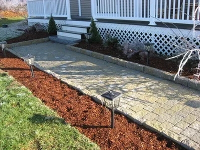 Installed paver patio with mulch beds and metal landscape edging adjacent to residential deck