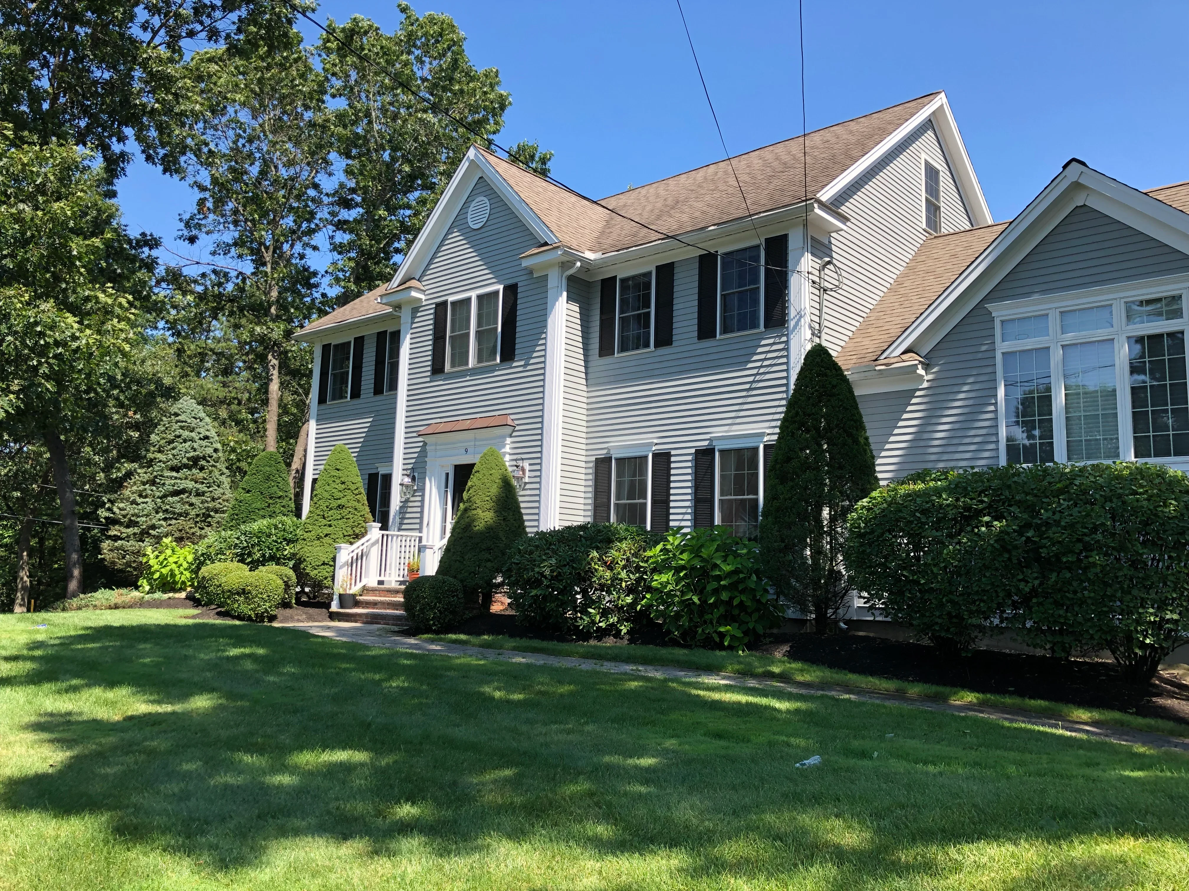 Manicured evergreen shrubs and foundation plantings around colonial home with white siding