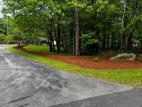 Red mulch bed with landscape edging along tree line, freshly installed