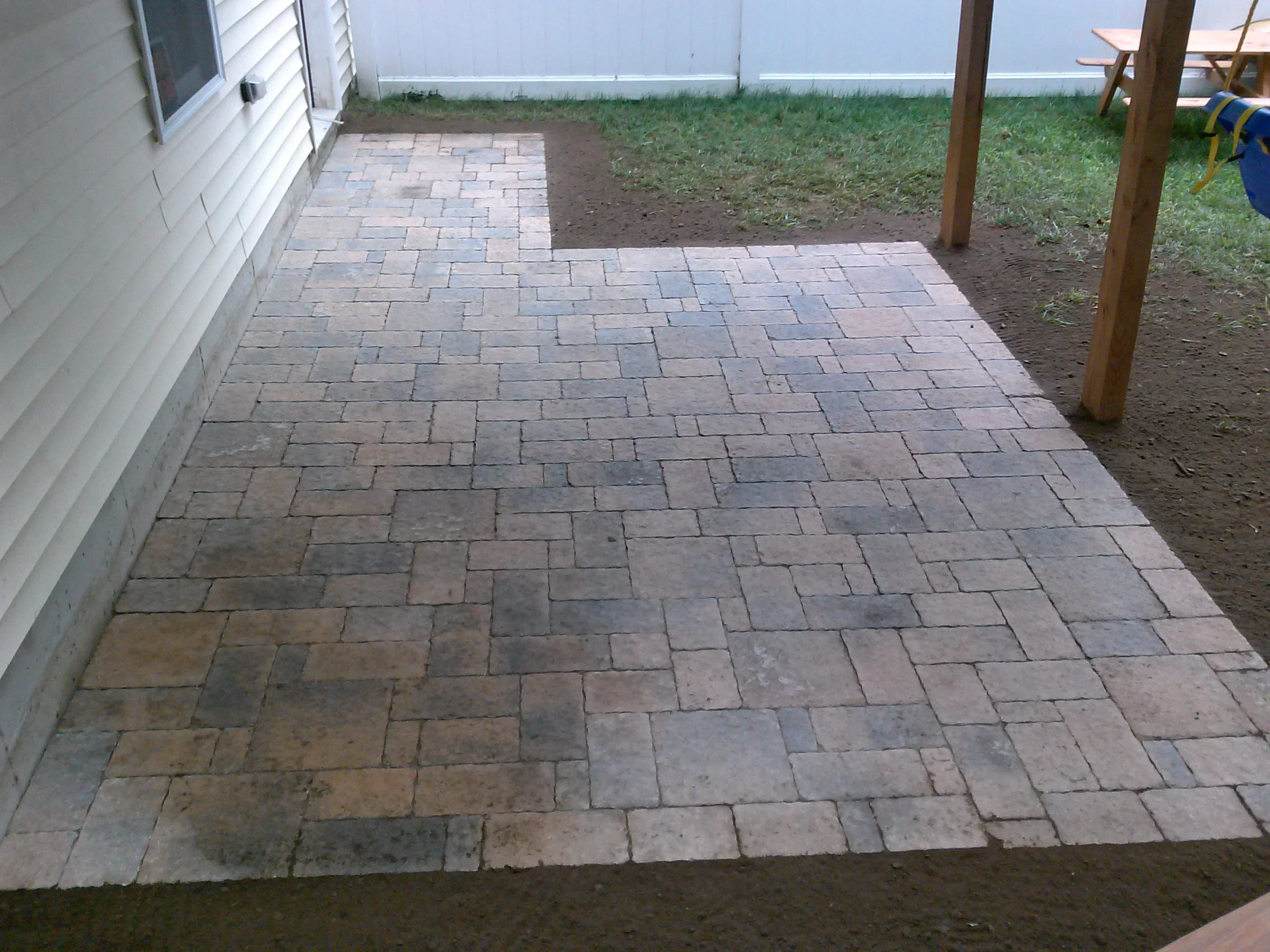 Completed permeable paver patio with running bond pattern in earth tones, installed next to white house siding
