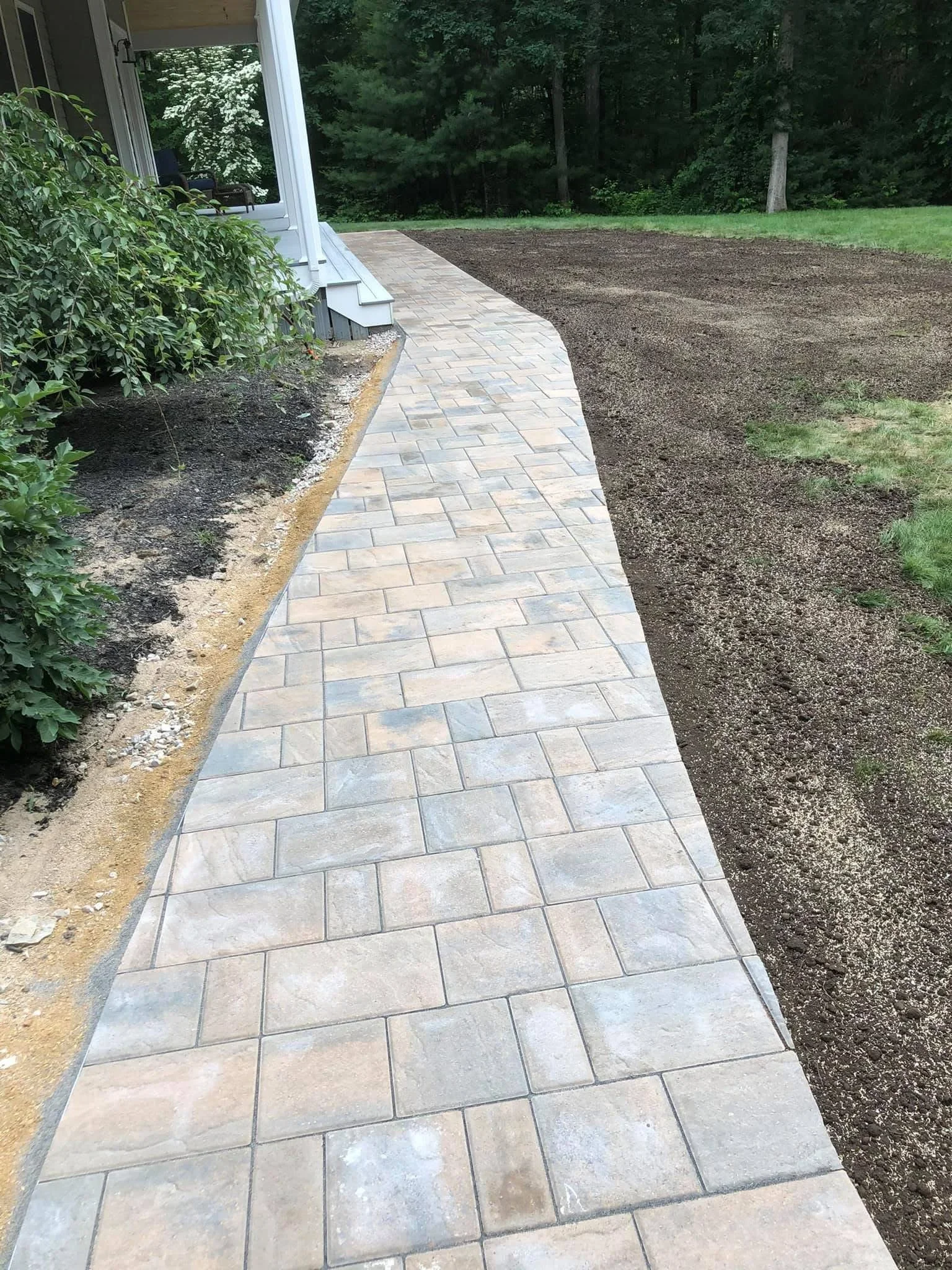 Curved concrete paver walkway with running bond pattern and adjacent mulched landscape bed with metal edging