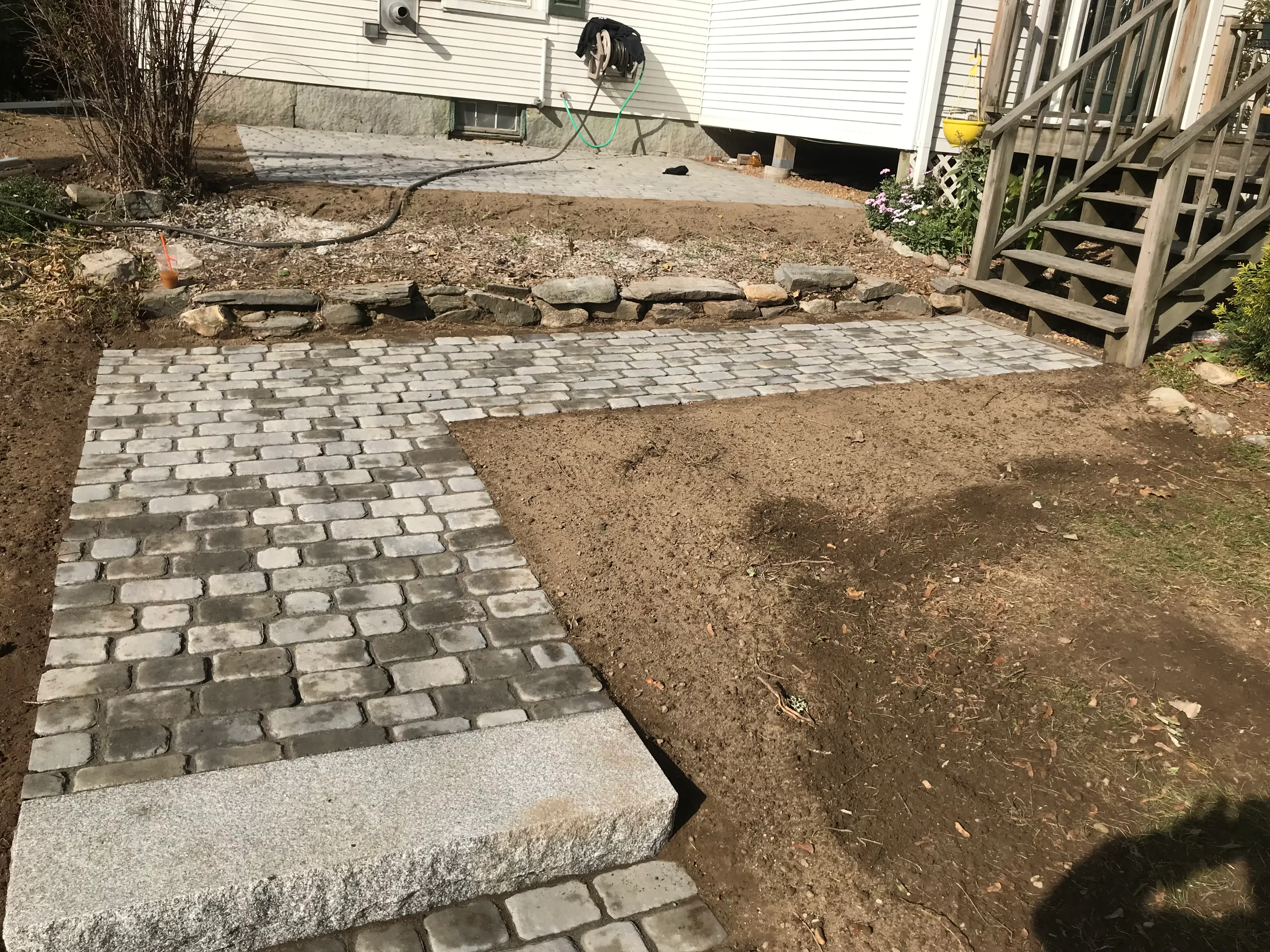 Gray and tan concrete pavers in running bond pattern with stone border during installation