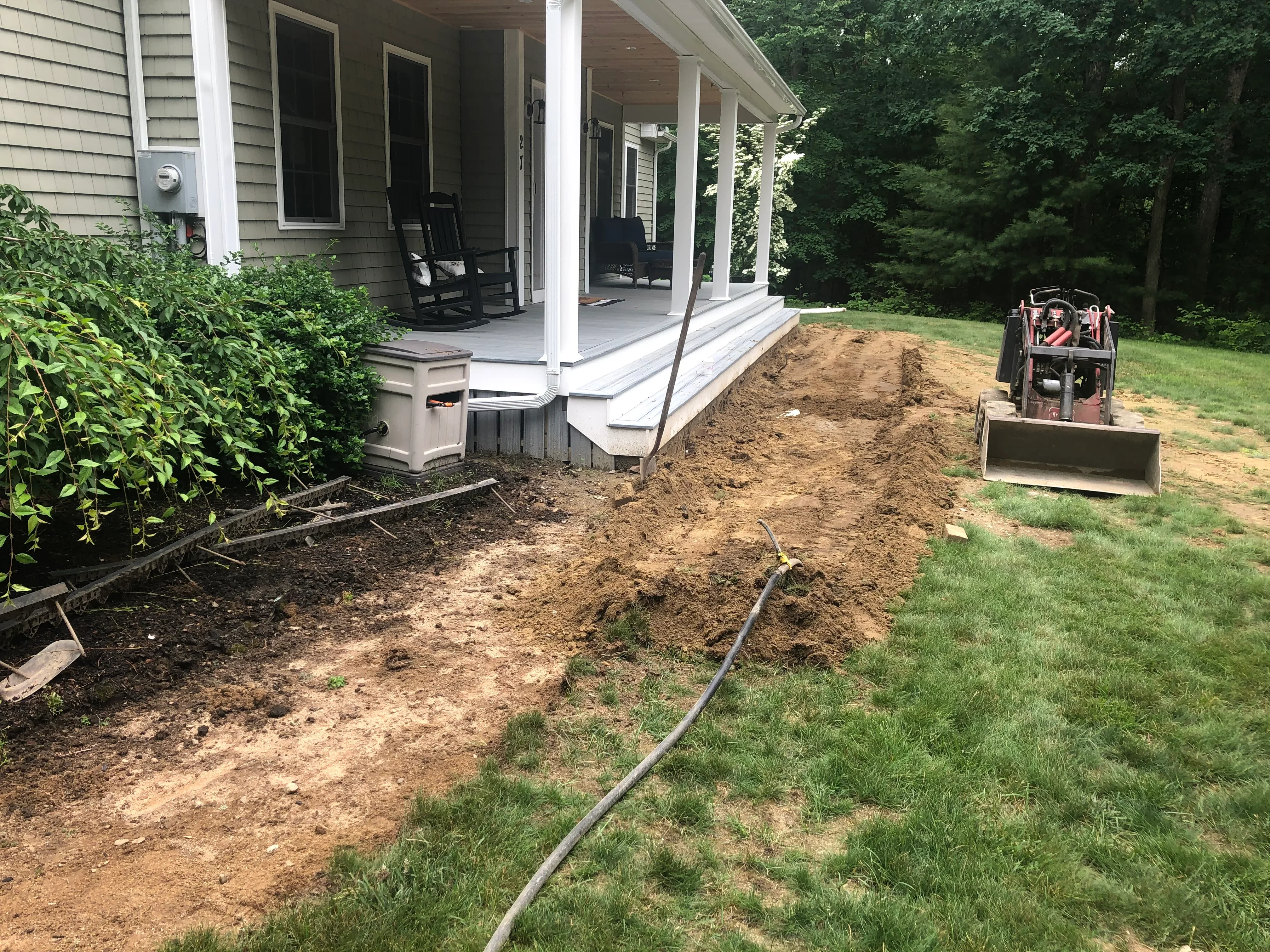 Graded dirt yard with mini excavator, drainage pipe, and prepared soil near residential porch